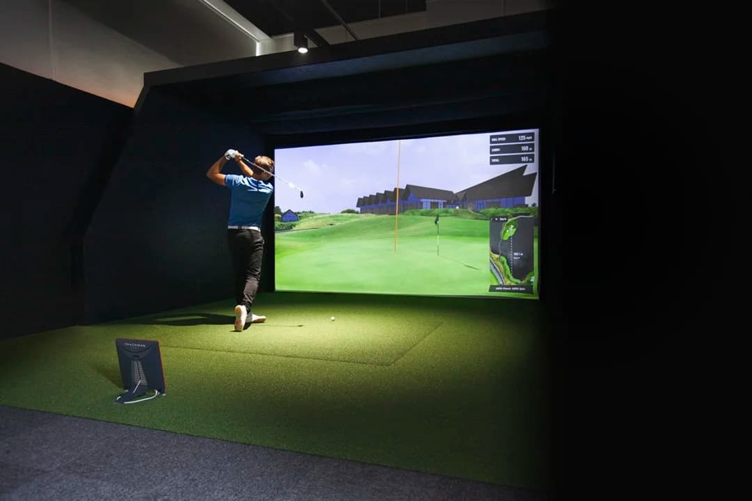 Golfer swinging in TrackMan bay with course data on screen